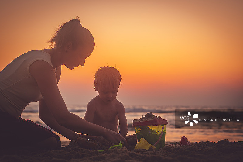 母亲和儿子在日落的沙滩上玩沙子图片素材