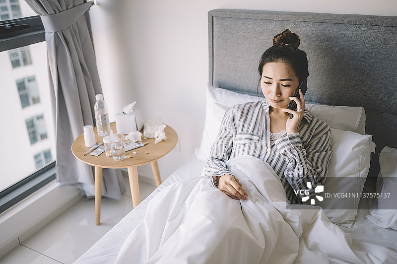 一位亚洲华人女性穿着睡衣在卧室的床上讲电话图片素材