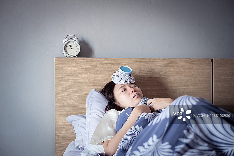 亚洲妇女感冒高烧，睡在舒适的床上使用冰袋受伤减少。生病在家图片素材