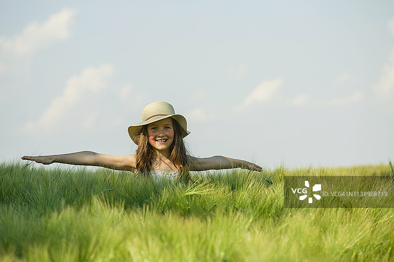 肖像无忧无虑的女孩与双臂伸展在阳光下，农村绿色的田野图片素材