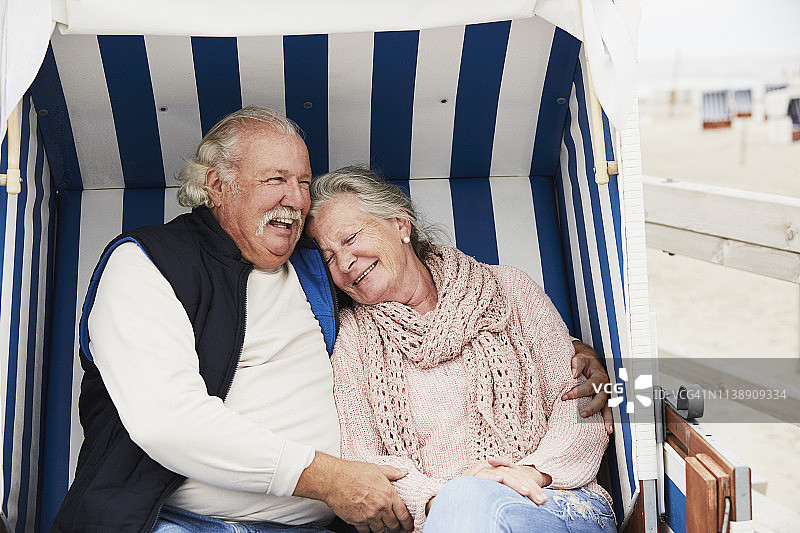 一对老年夫妇坐在海滩上的兜帽沙滩椅拥抱的肖像图片素材