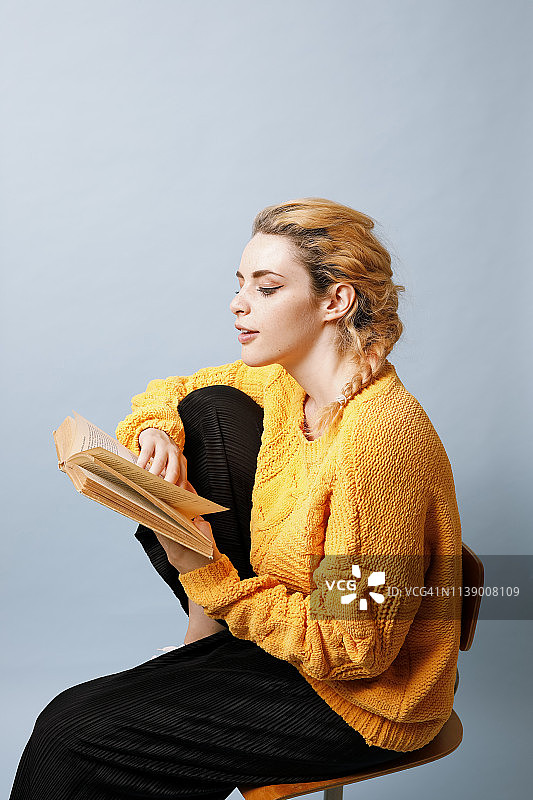 年轻女子穿着黄色针织套衫在蓝色背景前看书图片素材