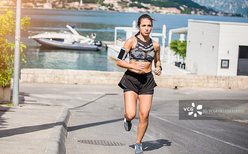 一个夏日里，运动的年轻女子在海边的一条路上跑步。图片素材