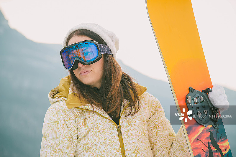 女人拿着滑雪板，背景是高山图片素材