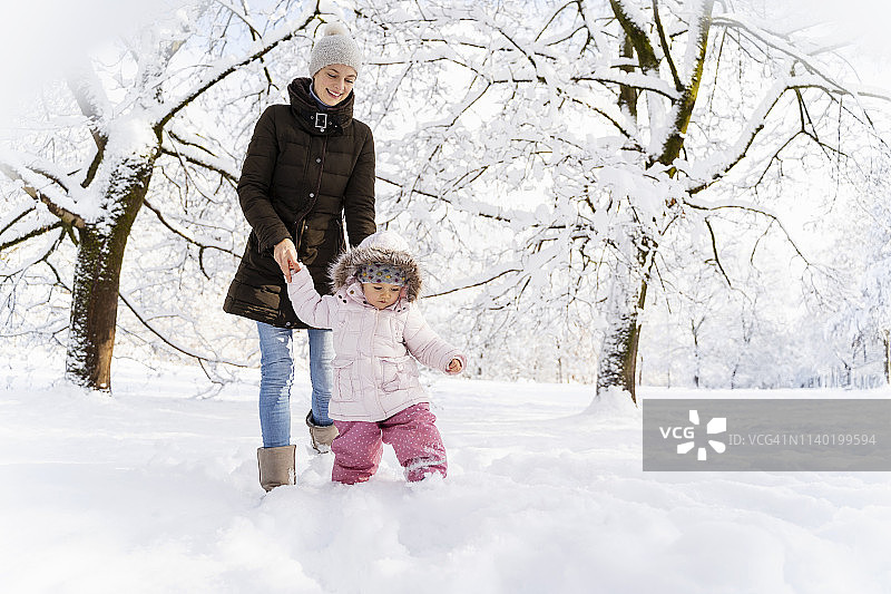 快乐的母亲和女儿在冬天的风景中散步图片素材