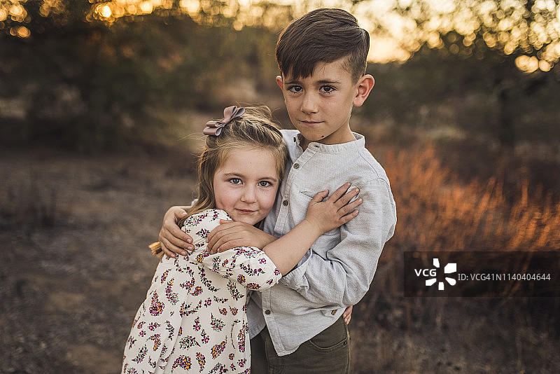 日落时分，小女孩和小男孩在加州田野里拥抱图片素材
