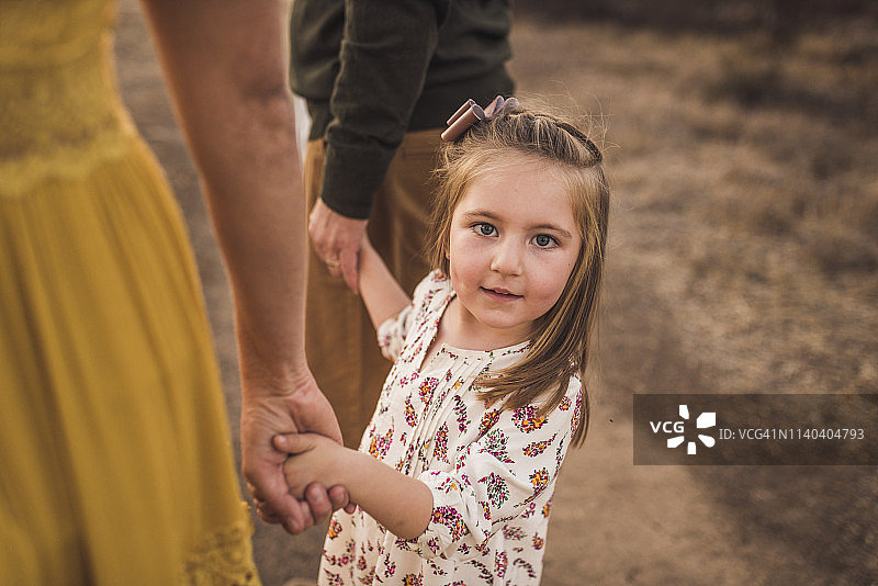 日落时分，小女孩牵着父母的手在加利福尼亚的田野里图片素材