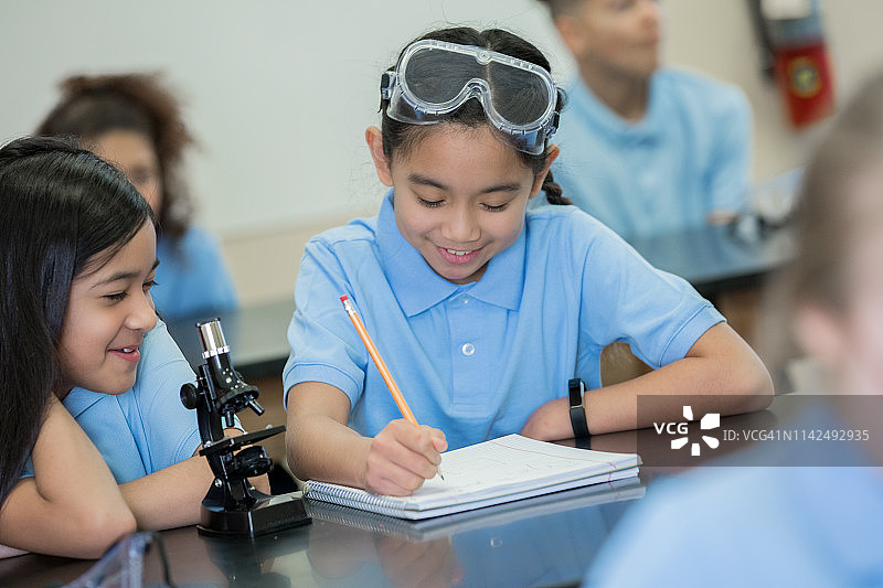美丽的小学生小女孩微笑着在STEM课堂上使用显微镜图片素材