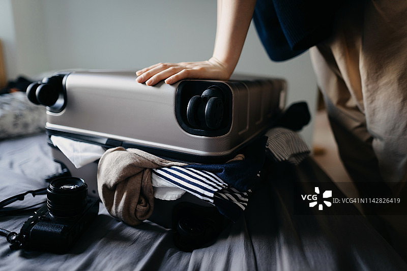 女人为度假打包手提箱，挣扎着在家里的床上装满手提箱图片素材