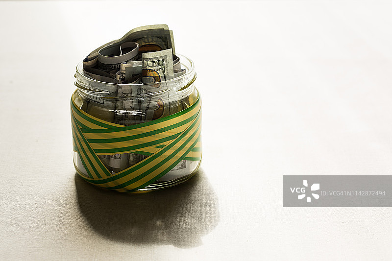 装着美钞的罐子，用黄绿条纹胶带包裹图片素材