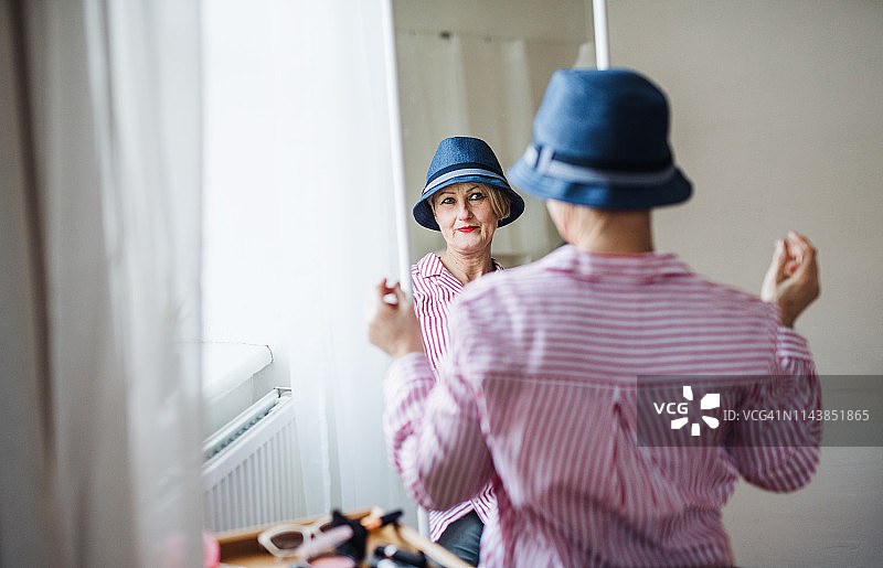 一名活跃的老年妇女在试着戴一顶新帽子，看着镜子的背影。图片素材