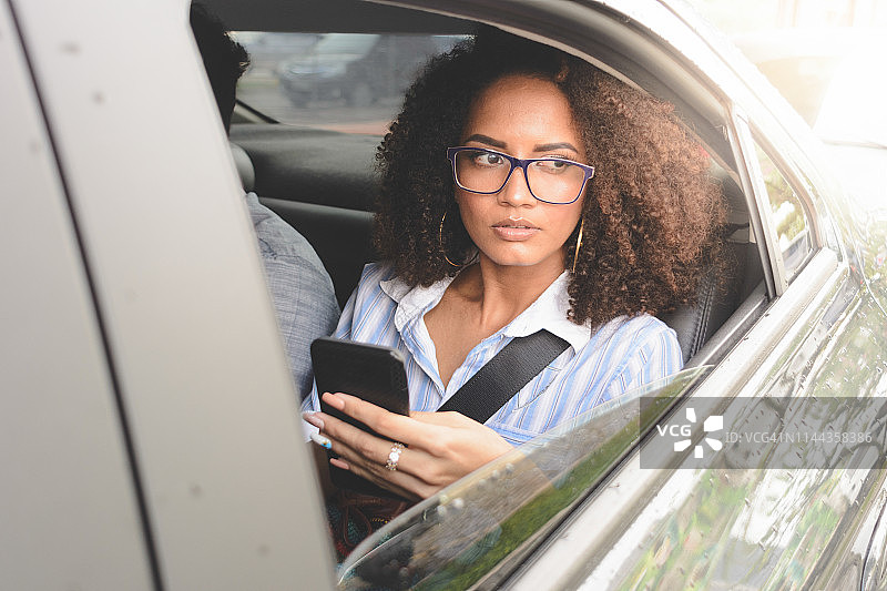 一名女子在汽车后座上用智能手机向外看图片素材
