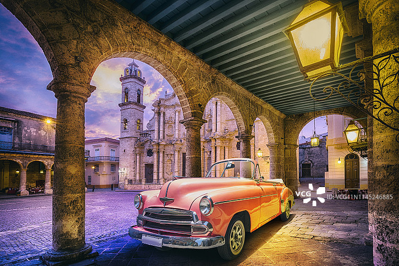 在黎明时分，一辆老式的粉红色敞篷车穿过古巴哈瓦那老城图片素材