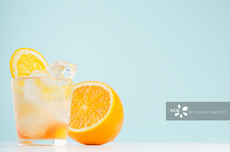 新鲜橙条鸡尾酒与烈酒，块橙，冰块优雅的软蓝色墙壁和白色木桌。图片素材