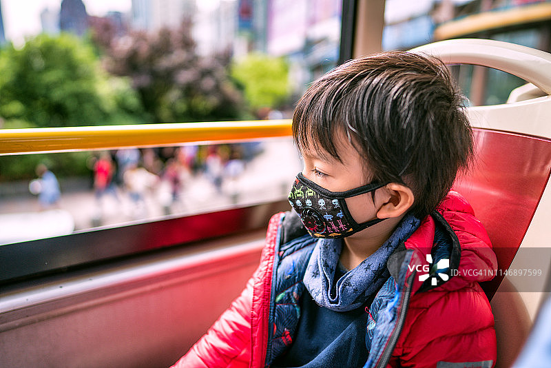 一个戴着防护口罩的小男孩坐在观光巴士上的肖像，黄浦区人民广场，中国上海图片素材