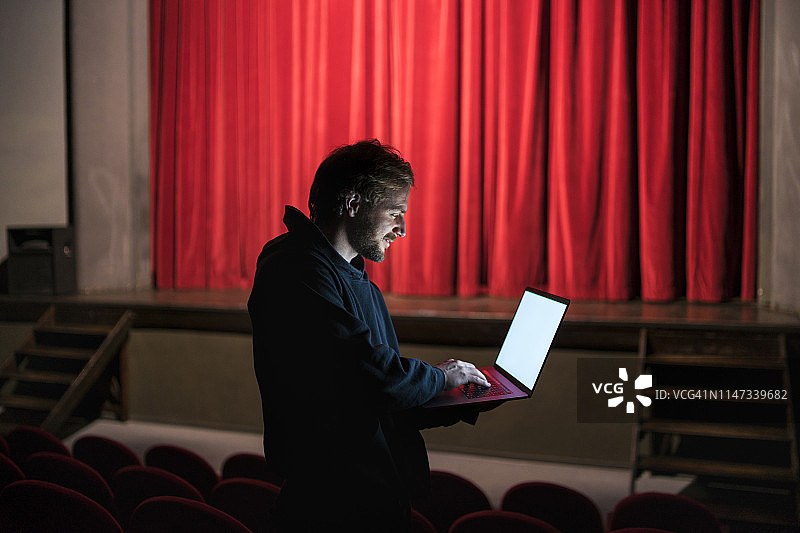 导演站在剧院礼堂使用笔记本电脑图片素材