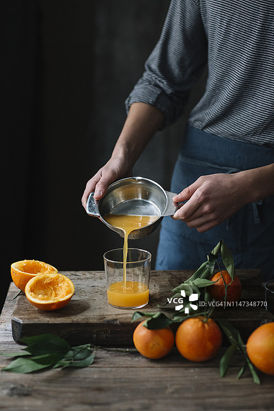 年轻男子将鲜榨的橙汁倒进玻璃杯，局部视图图片素材