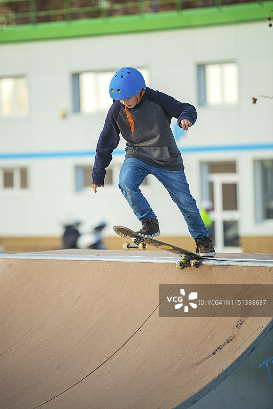 戴着蓝色头盔的年轻溜冰者准备在滑板坡道上表演一个戏法图片素材