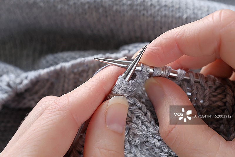 在女孩手中残缺的项目编织和金属编织针特写。女人织一件灰色羊毛衫。爱好的概念，创造力，针线活，手工。图片素材