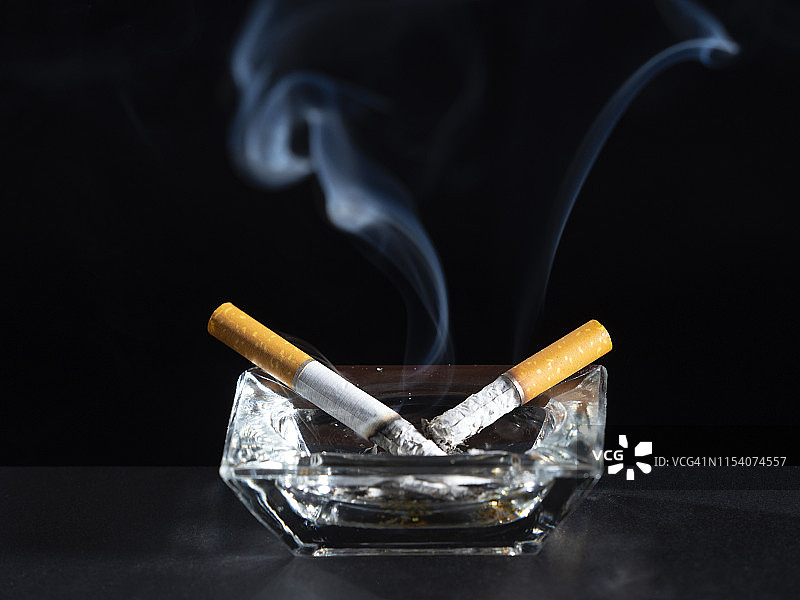 黑色背景上的烟灰缸内点燃的香烟有烟迹。图片素材