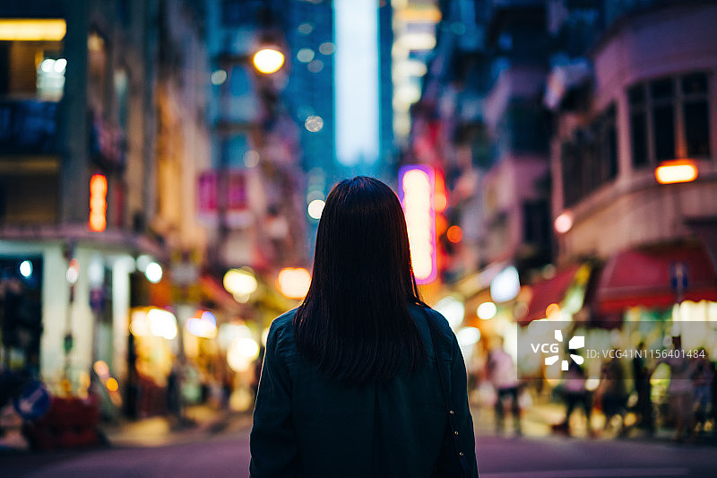 在城市的年轻女子的后视图，站在灯光照亮的城市街道在黄昏图片素材