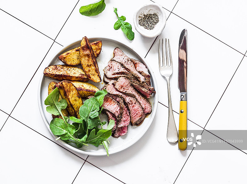 牛排和烤新土豆-美味的午餐在一个明亮的背景，俯视图图片素材