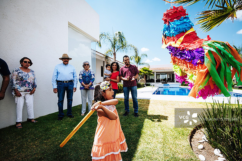 拉丁小女孩带着家人，在豪宅的后院打piñata。图片素材