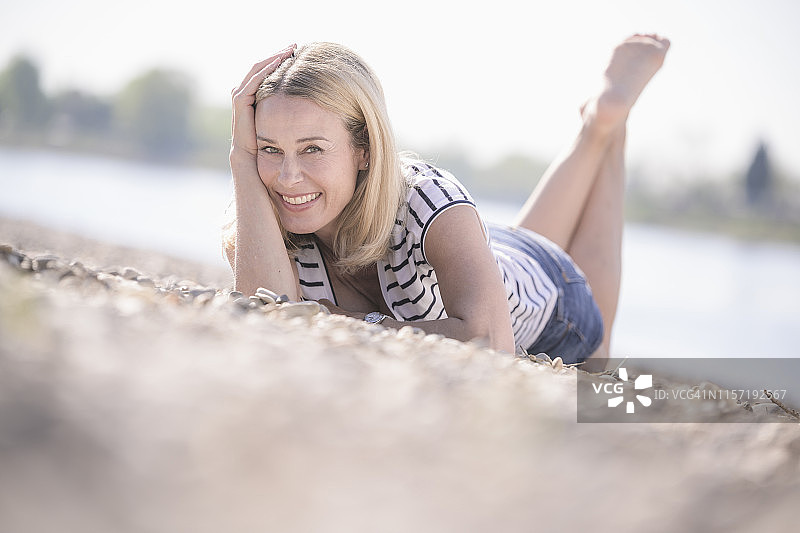 微笑着的成熟女子躺在河边的卵石上图片素材