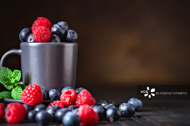 深色背景上的杯子里的覆盆子和蓝莓。夏日与健康的饮食理念。背景与复制空间。有选择性的重点。水平的。图片素材