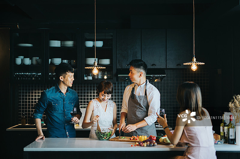 一群快乐的年轻亚洲男女在厨房里一起做饭，一边准备派对食物，一边愉快地聊天，享受红酒图片素材