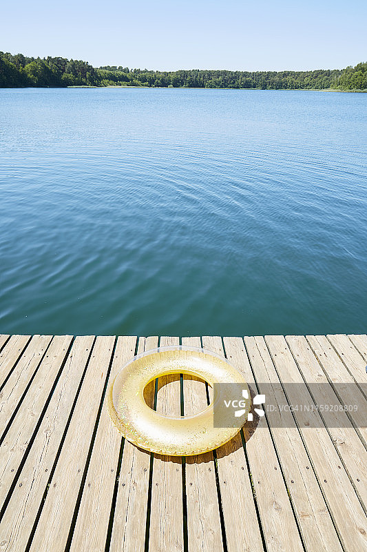 湛蓝的天空下，田园诗般的湖上的码头上的金色充气圈图片素材