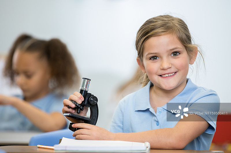 在STEM课堂上，一个可爱的小女孩穿着私立学校的校服使用显微镜图片素材