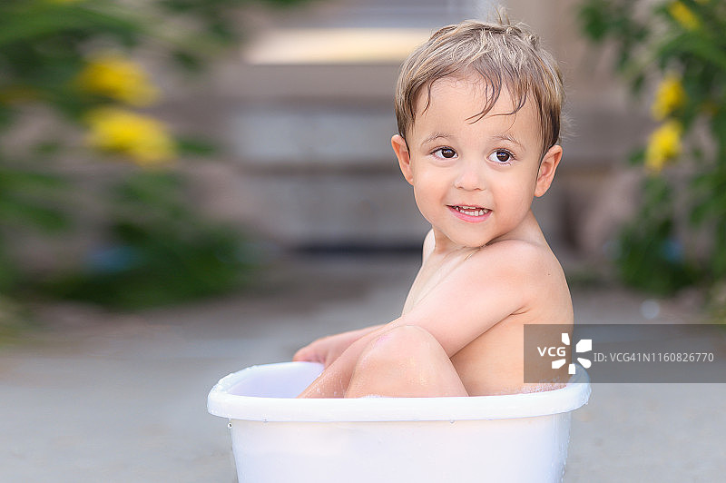 3岁的小孩坐在小桶水里在户外洗澡图片素材