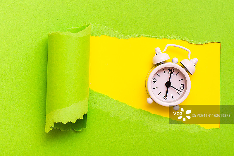 闹钟在一个洞里，绿色的纸上，黄色的背景。图片素材