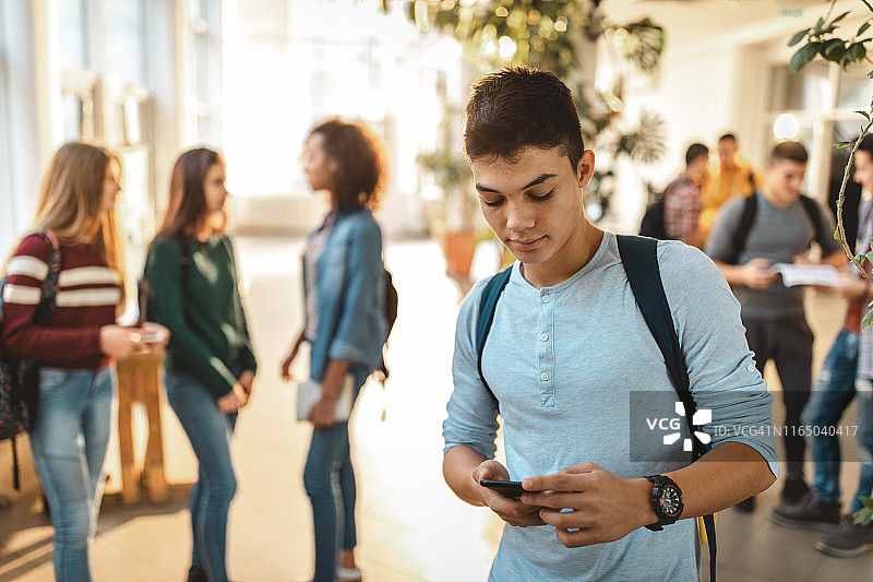 一名男高中生在学校走廊里使用手机。图片素材