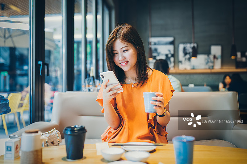 年轻的亚洲女性使用智能手机做生意，网上购物，转账，金融，网上银行。在咖啡店咖啡店模糊的背景。图片素材