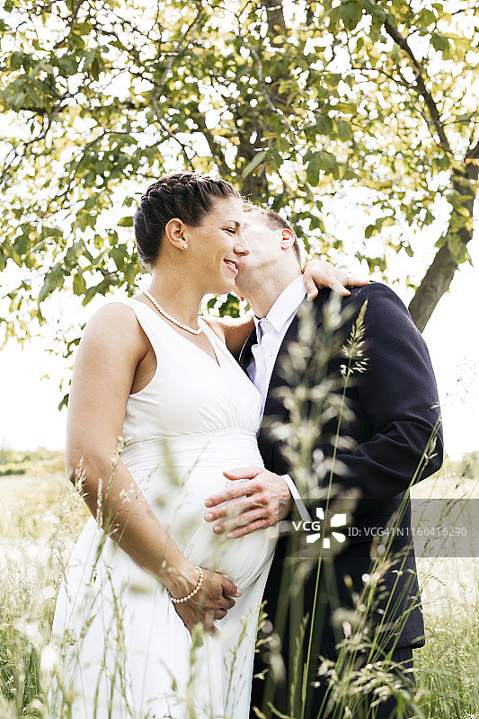 怀孕的新娘和她的丈夫抱着小宝宝在草地上图片素材