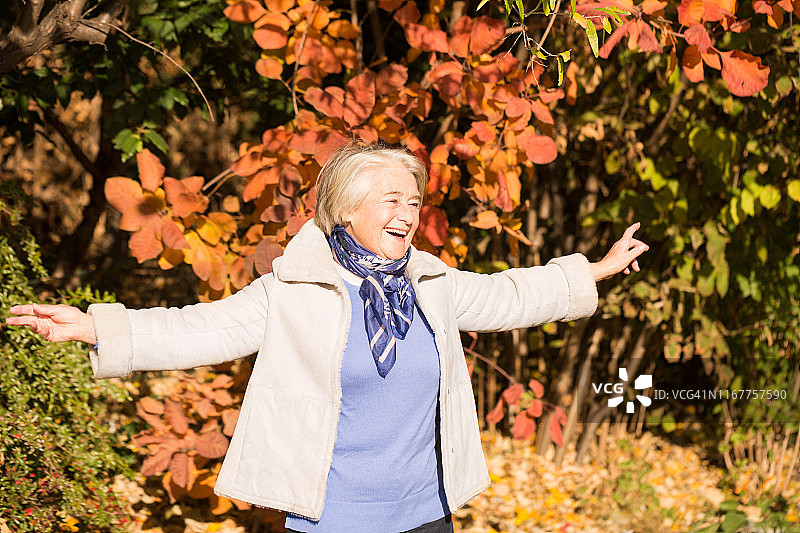 一个美丽的微笑奶奶的手臂在秋天的颜色在自然展开。图片素材