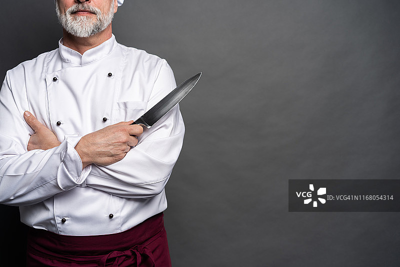 一个成熟的厨师厨师的肖像拿着刀孤立在一个黑色的背景。图片素材