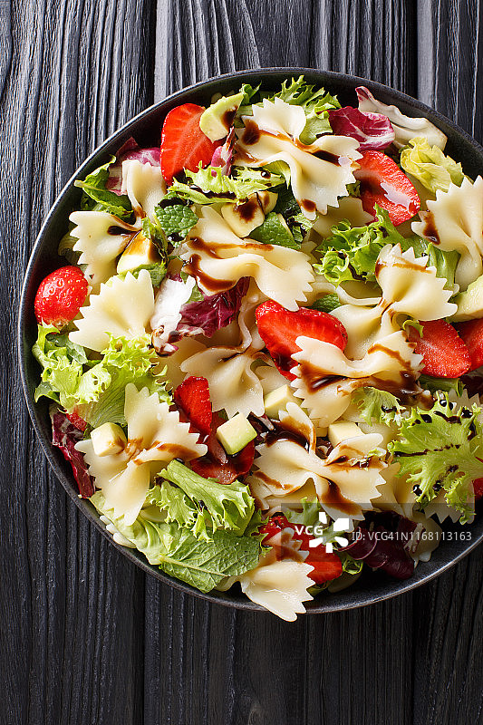 法法尔意大利面，鳄梨，草莓，混合生菜和香醋酱近距离放在盘子上。垂直的俯视图图片素材
