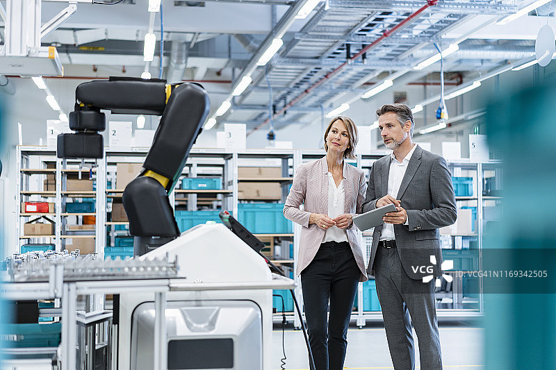 商人和女商人在一个现代化的工厂大厅看着机器人图片素材