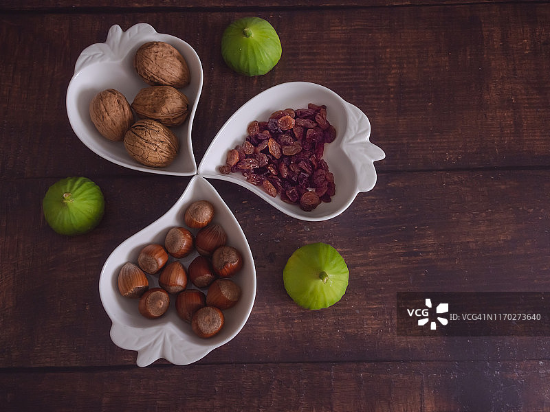 秋天的水果:一堆坚果、榛子、无花果和葡萄干，放在一个旧木桌上的心形瓷碗里图片素材