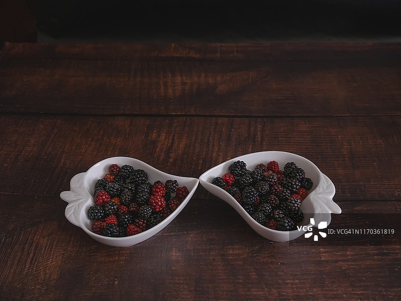 秋天的水果:黑莓放在旧木桌上的两个心形瓷碗里图片素材