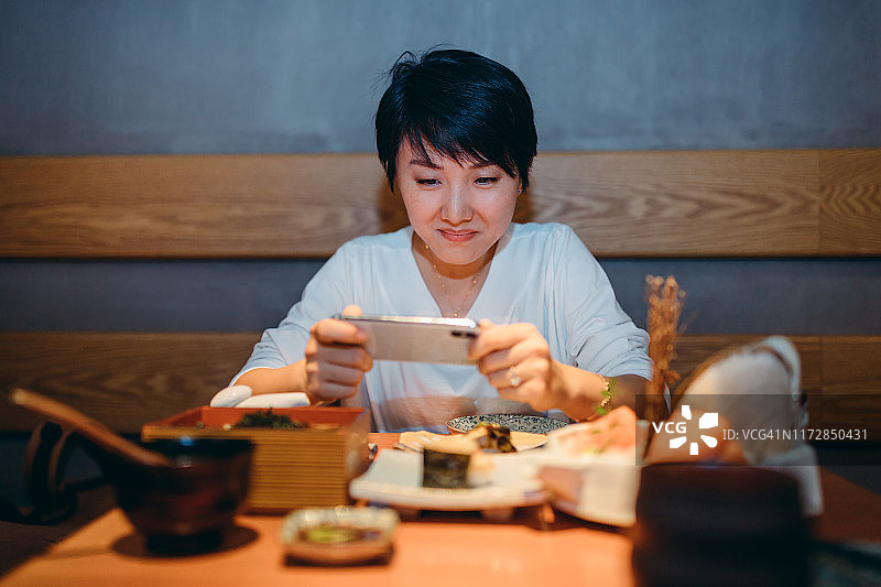 亚洲年轻女子在餐厅用手机拍摄她的新鲜日本食物的肖像。图片素材
