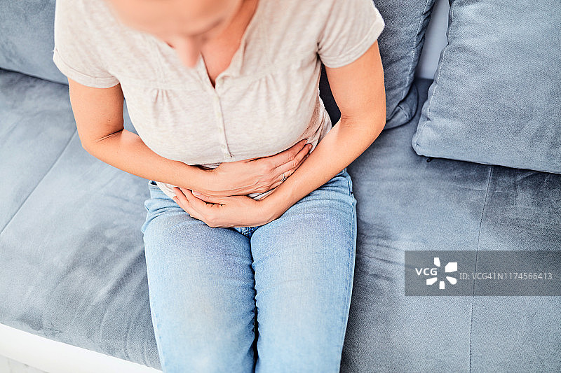 坐在沙发上时胃有问题的女人。图片素材
