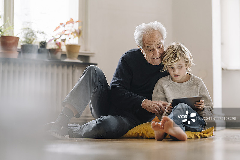 爷爷和孙子坐在家里的地板上使用平板电脑图片素材