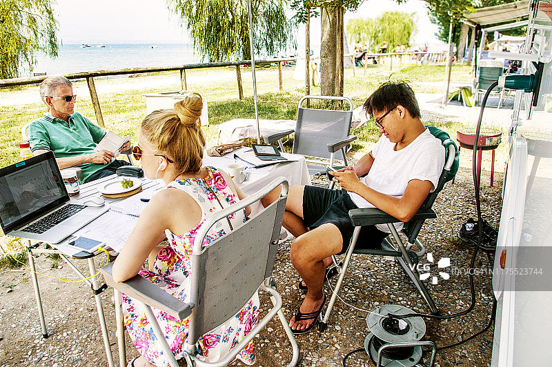 夏天，一家人围坐在湖边房车前的露营桌旁图片素材