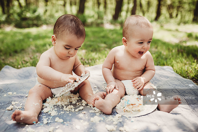 1岁的双胞胎兄弟在他们的第一个生日上只穿着尿布砸蛋糕图片素材