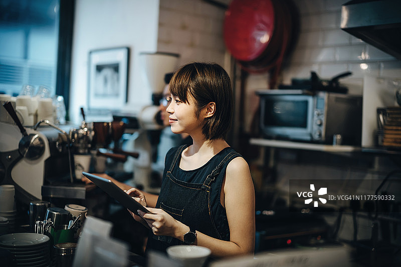 一名年轻的亚洲女咖啡师在一家咖啡店的吧台后面工作时使用数字平板电脑图片素材