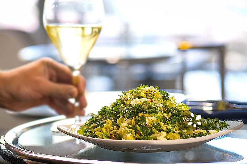 绿色沙拉和白葡萄酒被放在酒吧的玻璃桌上。图片素材